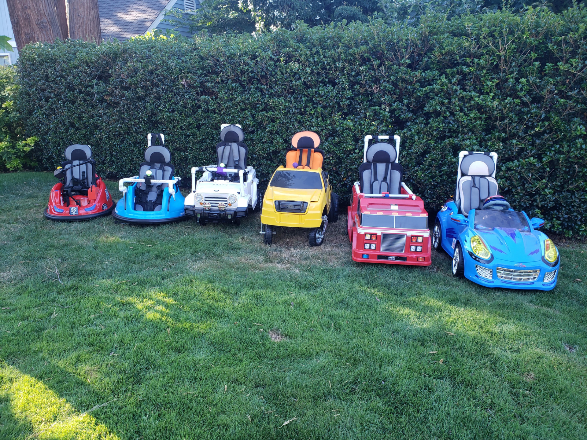 Six Wayfinder™ adapted ride-on cars lined up in a row on the lawn.